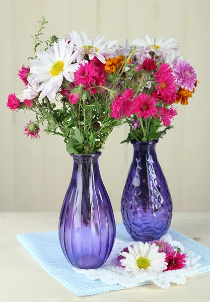 Wilde bloemen in glazen vazen op tafel op houten achtergrond — Stockfoto