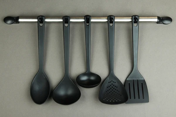 Plastic kitchen utensils on silver hooks on grey background — Stock Photo, Image