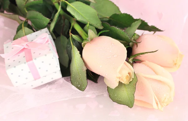 Beautiful roses and gift on pink cloth, close up — Stock Photo, Image