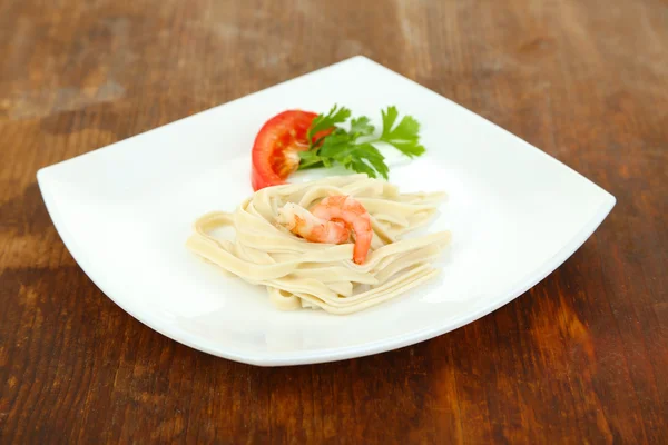 Pasta con gambas sobre plato blanco, sobre fondo de madera — Foto de Stock