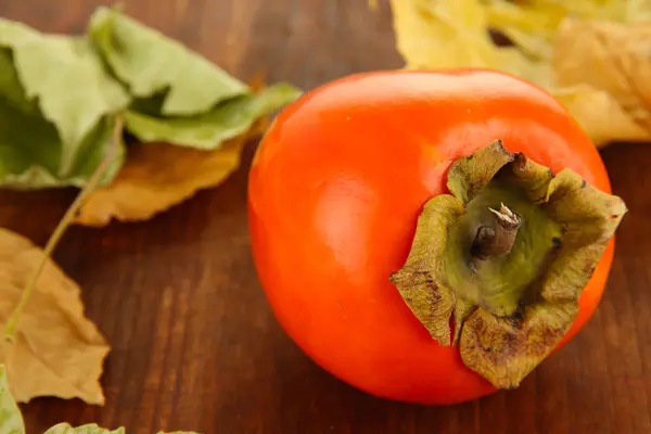 Rijp persimmon met gele bladeren op houten achtergrond — Stockfoto