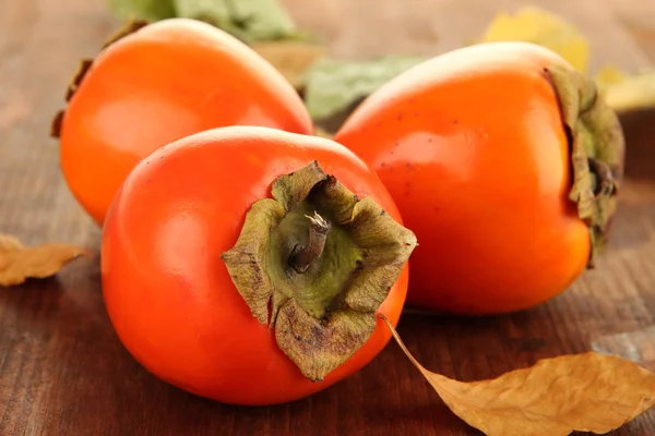 Persimmons mûrs avec des feuilles jaunes sur fond en bois — Photo