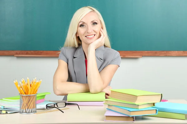 Professora da escola sentada à mesa no fundo do quadro negro — Fotografia de Stock