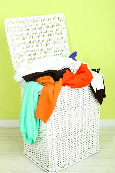 Full laundry basket on wooden floor on green wall background — Stock Photo, Image