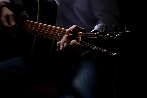 Junger Musiker spielt Akustikgitarre, Nahaufnahme, auf dunklem Hintergrund — Stockfoto