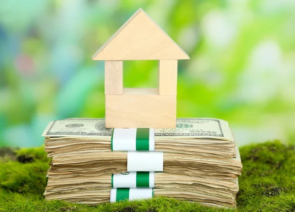 Wooden house on packs of dollars on grass on natural background — Stock Photo, Image