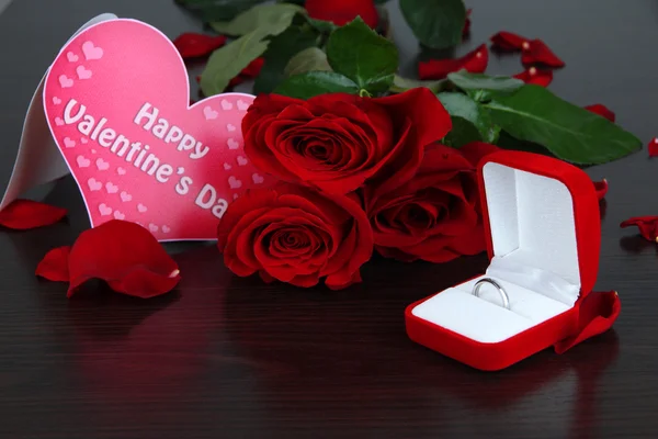 Ring surrounded by roses and petals on wooden table close-up — Stock Photo, Image