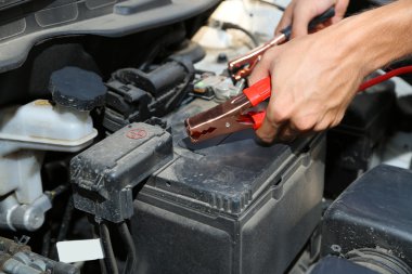 Car mechanic uses battery jumper cables to charge dead battery clipart