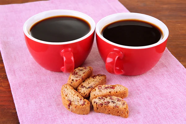 Red cups of strong coffee and cookies on napkin on wooden background — Stock Photo, Image