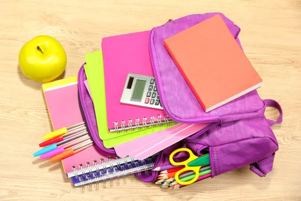 Purple backpack with school supplies on wooden background — Stock Photo, Image