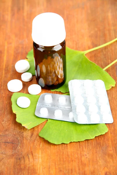 Ginkgo biloba folhas e garrafa de remédio em fundo de madeira — Fotografia de Stock