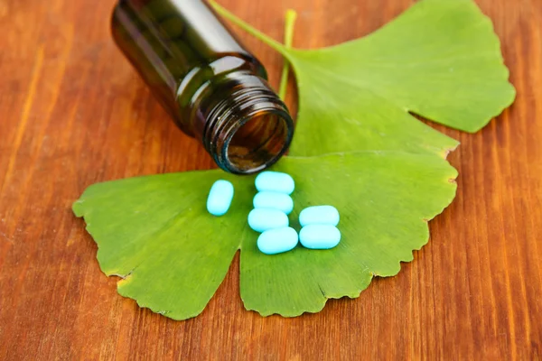 Feuilles de ginkgo biloba et bouteille de médicament sur fond en bois — Photo