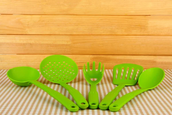 Plastic kitchen utensils on tablecloth on wooden background — Stock Photo, Image