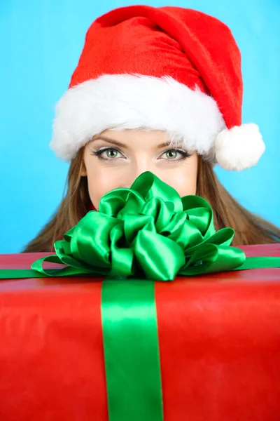 Красива усміхнена дівчина в новорічній шапці з подарунком на синьому фоні — стокове фото