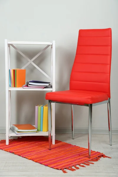 Interior bonito com cadeira de cor moderna, livros em suporte de madeira, no fundo da parede — Fotografia de Stock