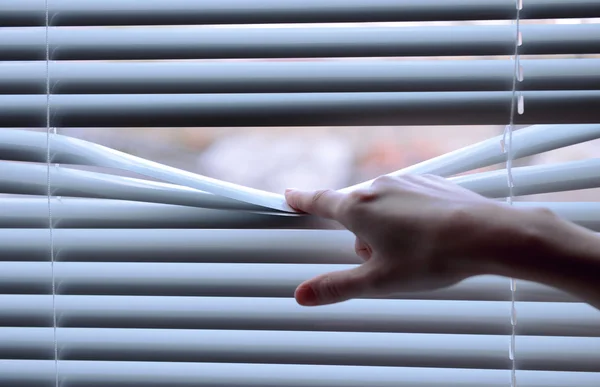 Female hand separating slats of venetian blinds with a finger to see through — Stock Photo, Image