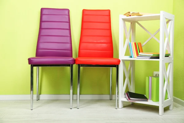 Beautiful interior with modern color chairs, books on wooden stand, on wall background — Stock Photo, Image