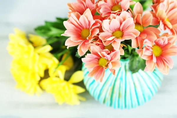 Όμορφα λουλούδια στο βάζο, σε ξύλινο τραπέζι, επάνω ελαφρύς υπόβαθρο — Φωτογραφία Αρχείου