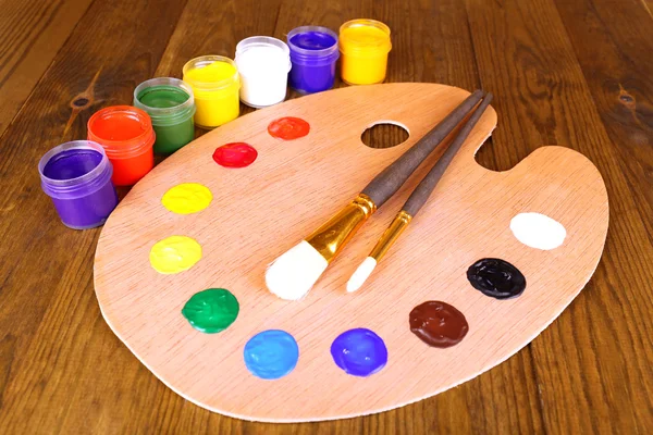 Wooden art palette with paint and brushes on table close-up — Stock Photo, Image