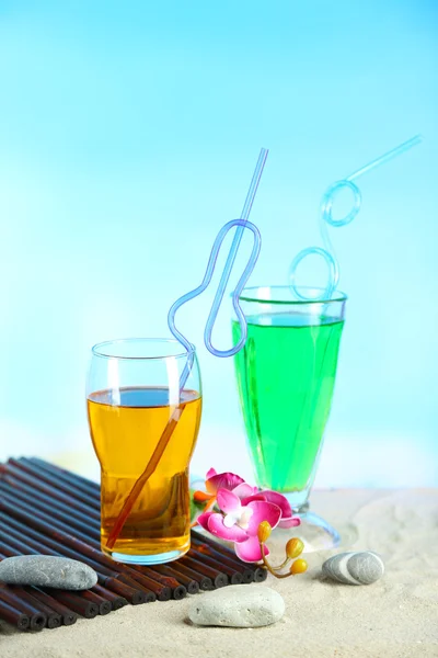 Glasses of cocktails on sand, on bright background — Stock Photo, Image