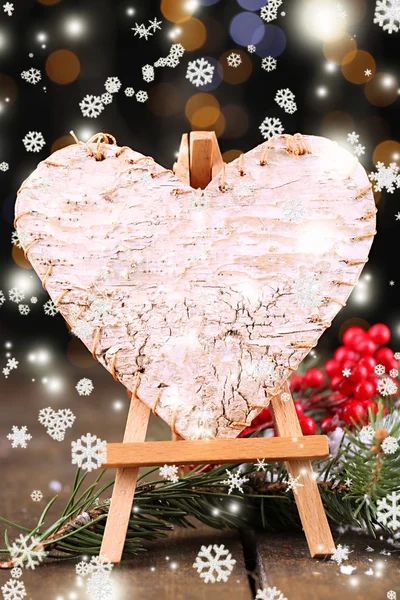 Corazón decorativo sobre caballete, sobre mesa de madera, sobre fondo brillante — Foto de Stock