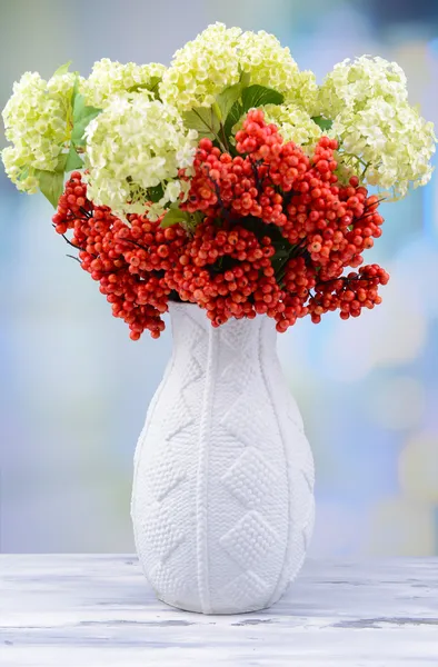 Blommor och bär i vas, på träbord, på ljus bakgrund — Stockfoto