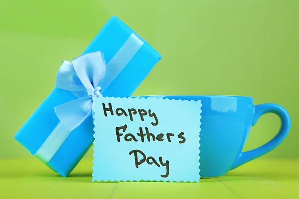 Happy Fathers Day tag with gift box and cup, on wooden table, on light background — Stock Photo, Image