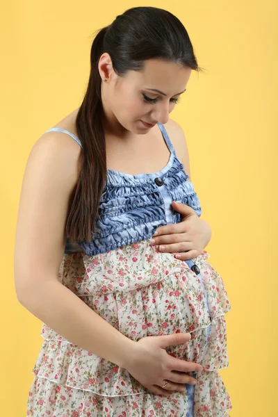 Beautiful young pregnant woman touching her belly on yellow background — Stock Photo, Image