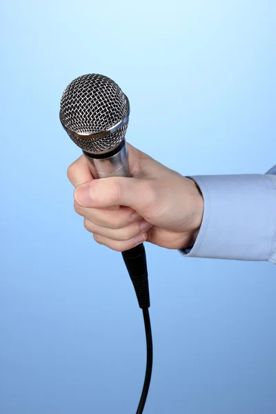 Male hand with microphone on blue background — Stock Photo, Image