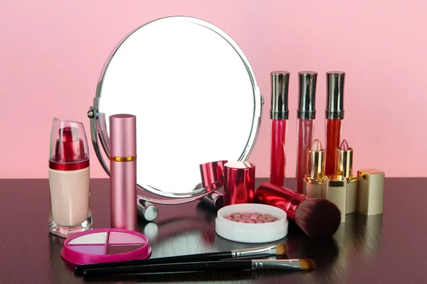 Espejo de mesa redonda con cosméticos sobre mesa sobre fondo rosa — Foto de Stock