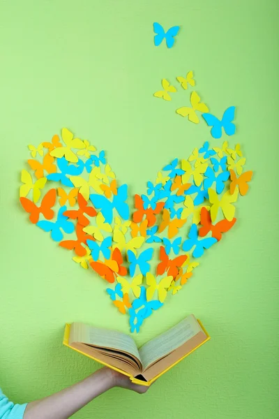 Paper butterflies fly out of book on green wall background — Stock Photo, Image