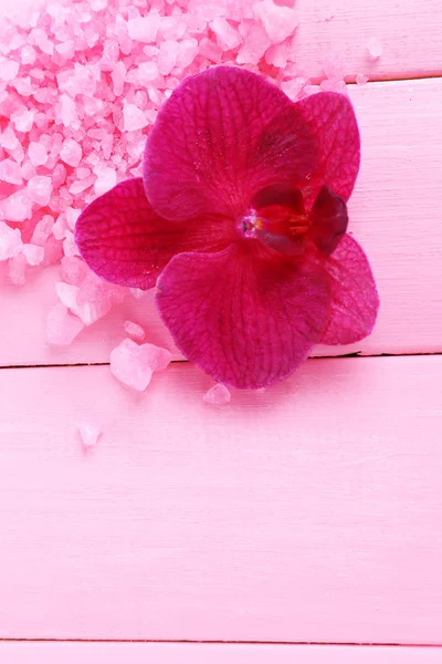 Beautiful blooming orchid flower and heap of sea salt, on color wooden background — Stock Photo, Image