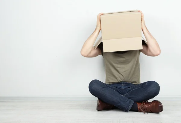 Hombre con caja de cartón en la cabeza sentado en el suelo cerca de la pared —  Fotos de Stock