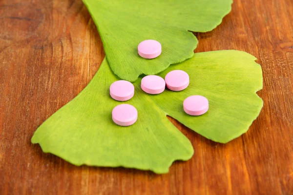 Ginkgo biloba leaves and pills on wooden background — Stock Photo, Image