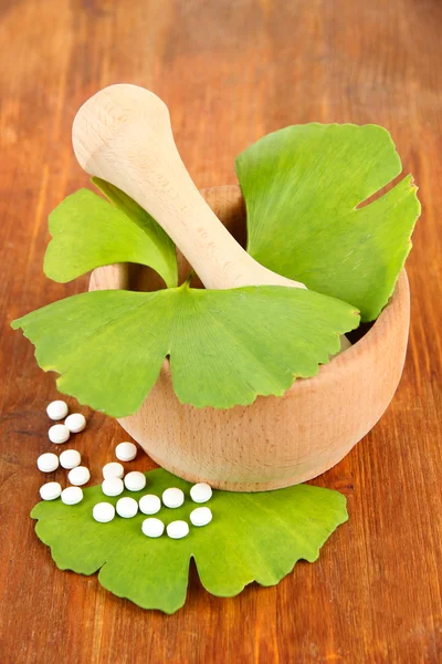 Ginkgo biloba leaves in mortar and pills on wooden background — Stock Photo, Image