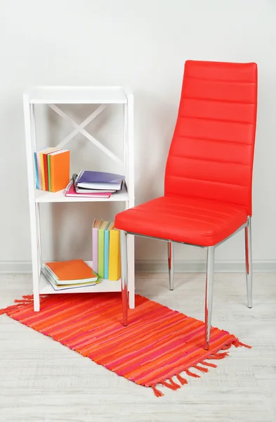 Interior bonito com cadeira de cor moderna, livros em suporte de madeira, no fundo da parede — Fotografia de Stock