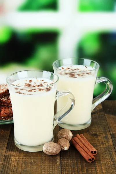 Cups of eggnog with cinnamon and nuts on table on bright background — Stock Photo, Image