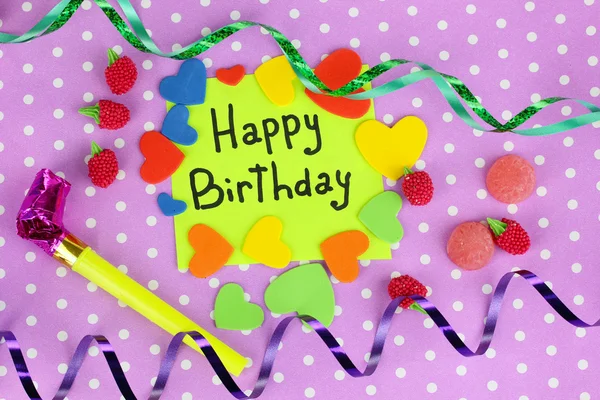 Carte "Joyeux anniversaire" entourée d'éléments festifs sur fond violet — Photo