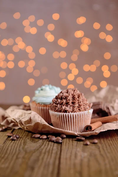 Gustosi cupcake con crema di burro, su tavolo di legno, su fondo luci — Foto Stock