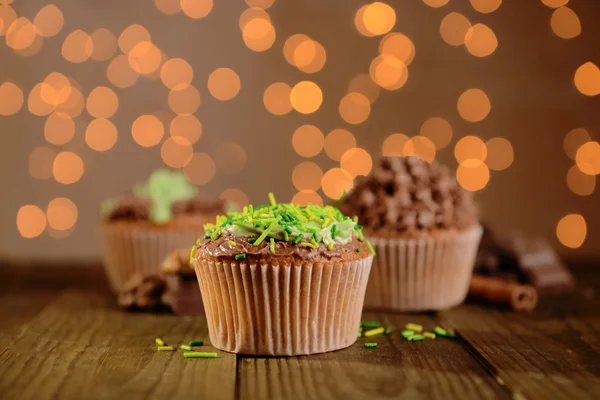 Sabrosos cupcakes con crema de mantequilla, sobre mesa de madera, sobre fondo de luces —  Fotos de Stock