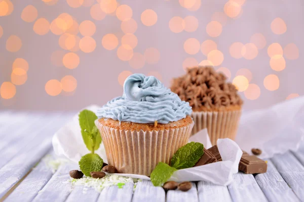 Tasty cupcakes with butter cream, on color wooden table, on lights background — Stock Photo, Image