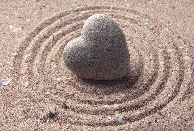 Grey zen stone in shape of heart, on sand background clipart