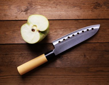 Mutfak bıçağı ve yeşil elma, ahşap arka planda.