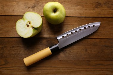 Mutfak bıçağı ve yeşil elma, ahşap arka planda.