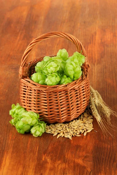 Verse groene hop in rieten mand en gerst, op houten achtergrond — Stockfoto