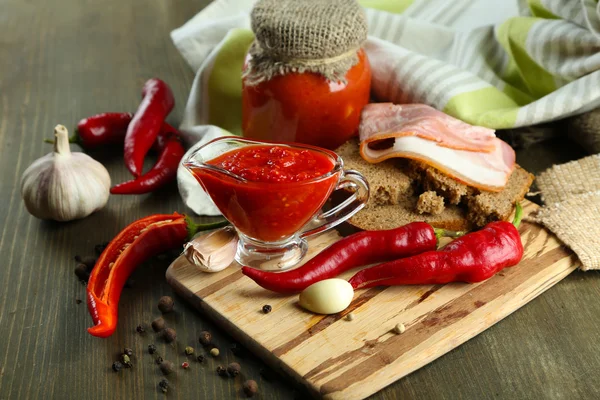 Composition with salsa sauce on bread,, red hot chili peppers and garlic, on napkin, on wooden background — Stock Photo, Image