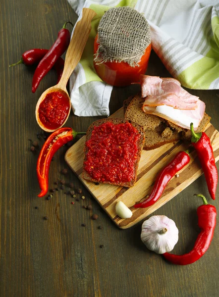 Composition with salsa sauce on bread,, red hot chili peppers and garlic, on napkin, on wooden background — Stock Photo, Image