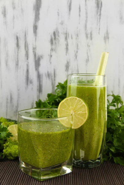 Glasses of green vegetable juice on bamboo mat on wooden background — Stock Photo, Image