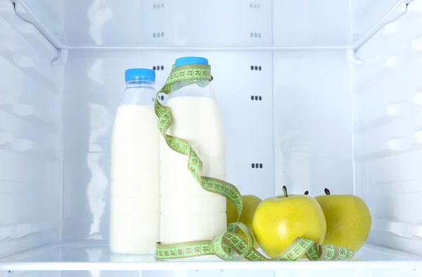 Conceptual photo of diet: apple and milk bottle with measuring type on shelf of refrigerator — Stock Photo, Image