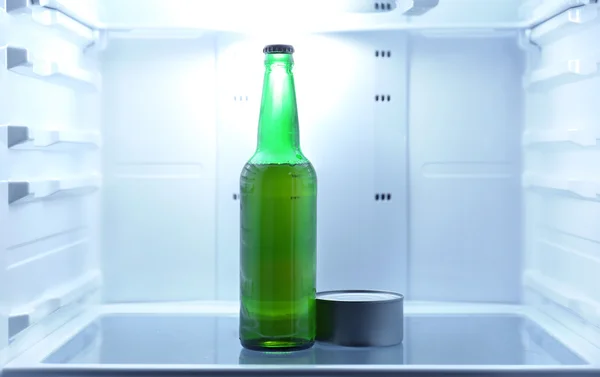 One beer bottle and canned tune in open empty refrigerator: bachelor fridge concept. — Stock Photo, Image